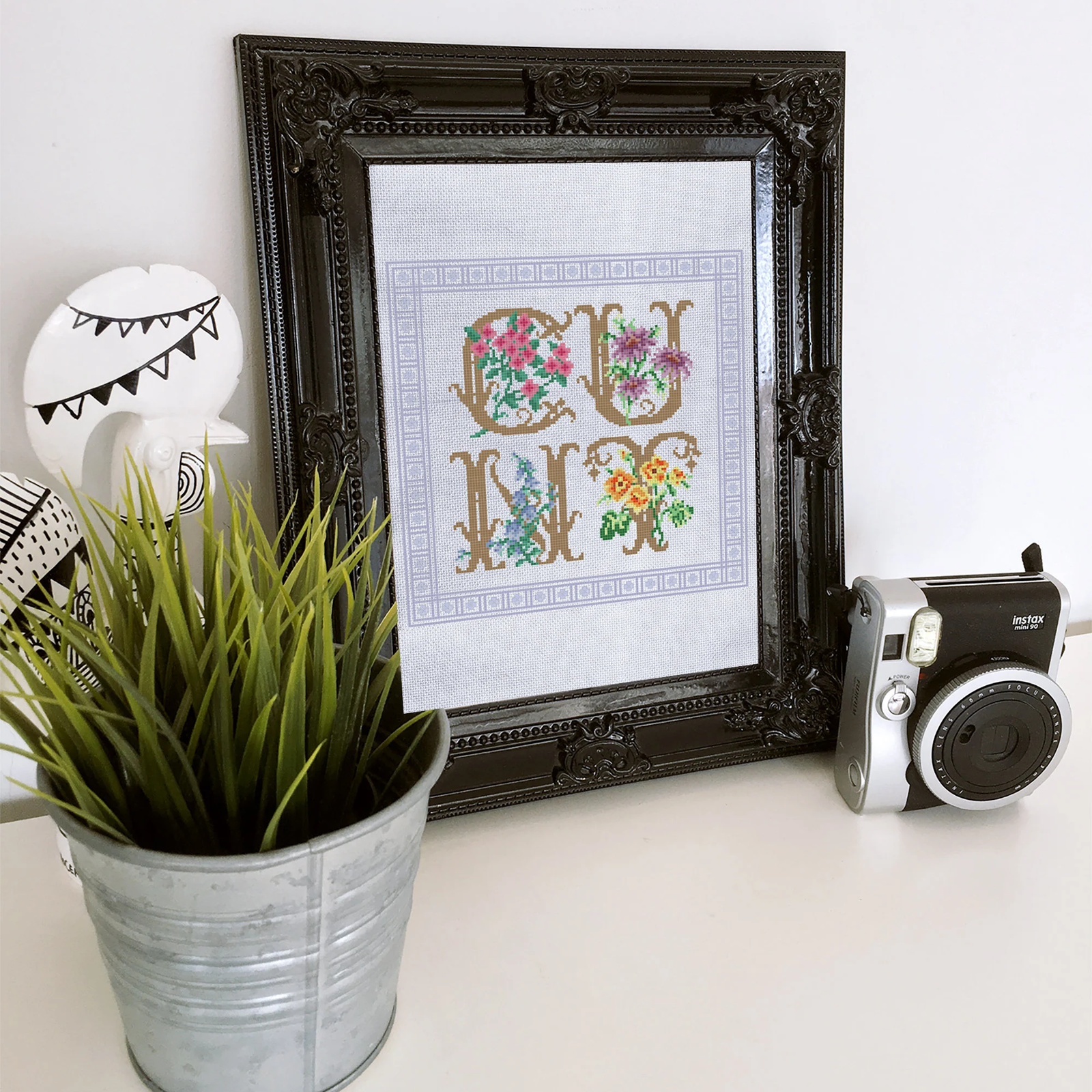 flowery cunt cross stitch example in a black frame sitting on a desk